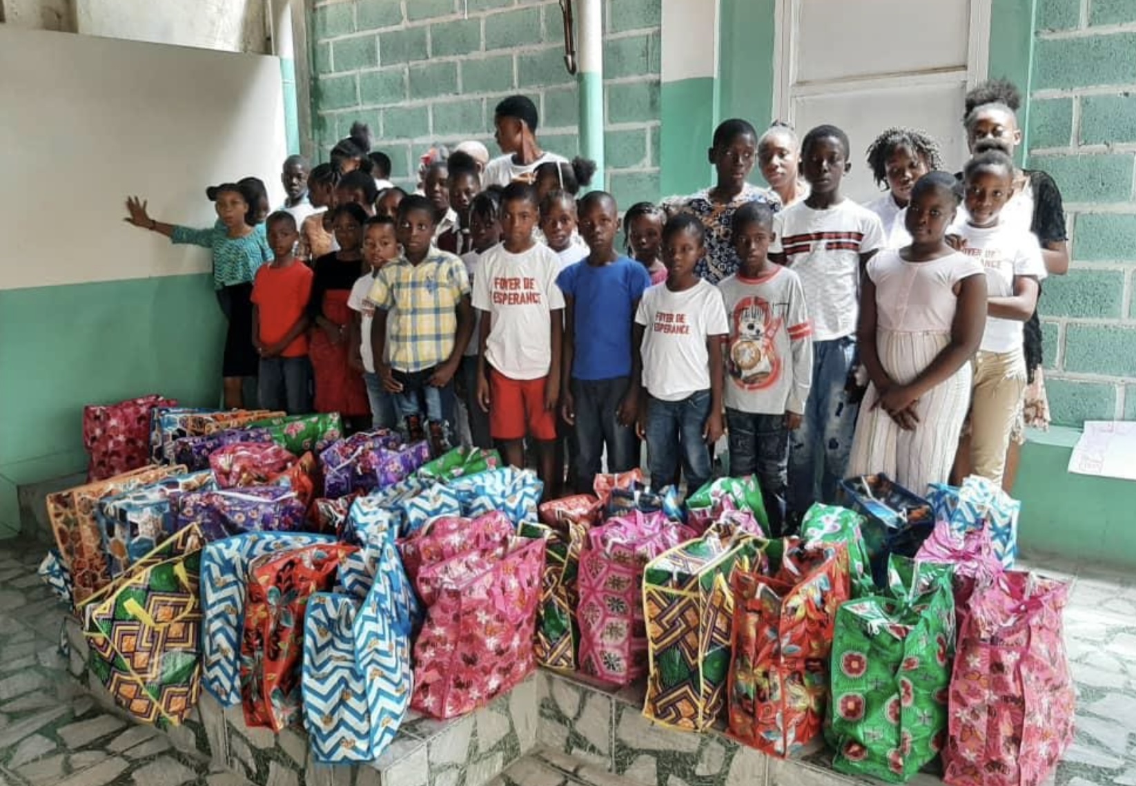 Des jeunes haïtiens devant de sacs contenant l’aide humanitaire © AED